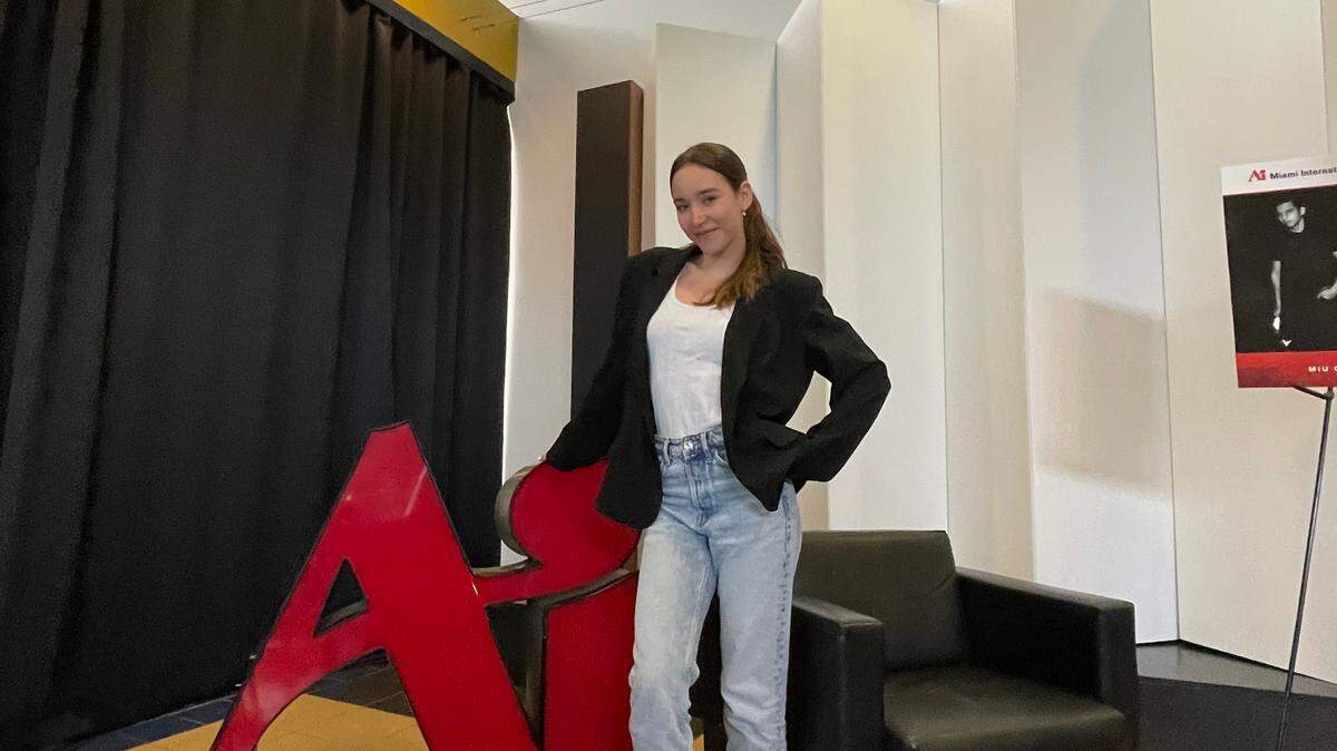 La estudiante de primer año Ana Beatriz Baú posa junto a un logotipo del Instituto de Arte en la Universidad Internacional de Arte y Diseño de Miami. La escuela cerrará abruptamente el sábado 30 de septiembre de 2023, dejando a estudiantes como ella en apuros. Cortesía de Ana Beatriz Baú.