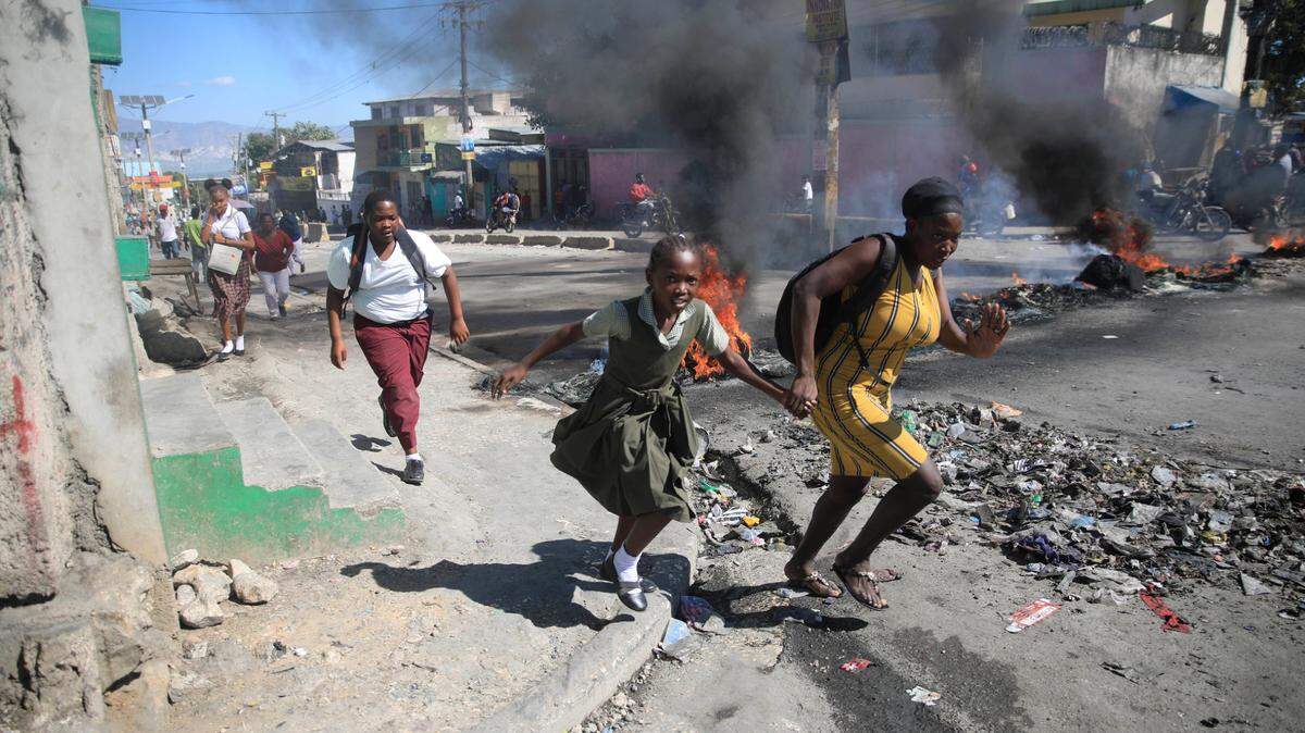 Una mujer con su hija pasa junto a una barricada levantada por policías en protesta por la mala gestión policial, en Puerto Príncipe, Haití, el jueves 26 de enero de 2023.