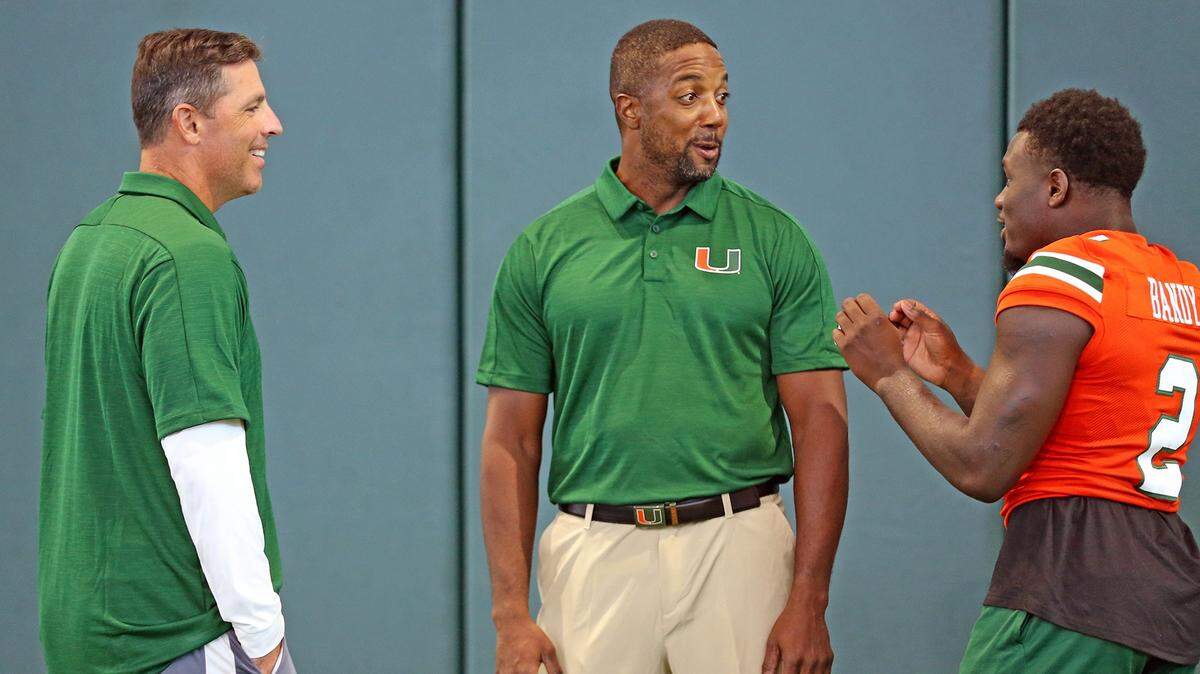 Miami Hurricanes offensive coordinator Dan Enos and cornerbacks coach Mike Rumph talk with cornerback Trajan Bandy (2) at media day at the University of Miami in Coral Gables, Florida, Tuesday, August, 13, 2019.