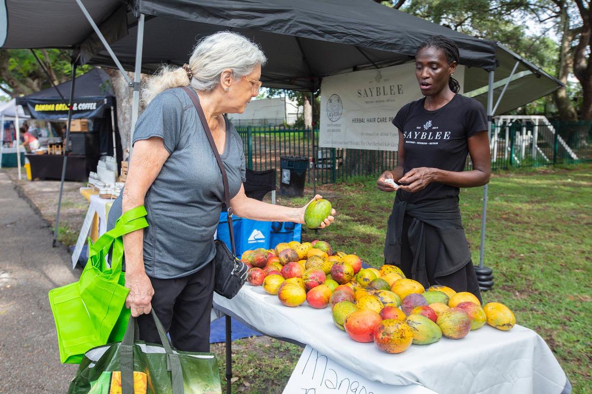 Debra Davies checks out mangoes at Sayblee Darsale’s table at Legion Park Farmer’s Market in Miami. Area farmers markets have mangoes, but they’re selling out quickly due to a shortage of fruit.
