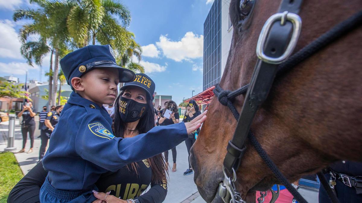 Jeremiah Valera, who just turned 5, with Silvia Vanni from the Mystic Force Foundation, meets Pouncer, a police horse, at the North Miami police station March 20, 2021. Jeremiah is battling cancer and wants to be a police officer. North Miami police, along with the Mystic Force Foundation, swore him in during a special ceremony.