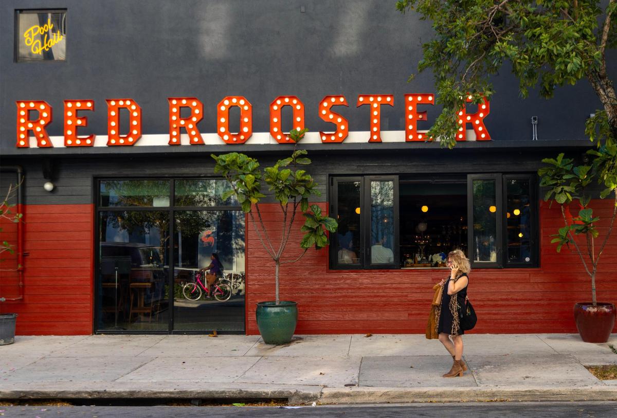 On Feb. 1, 2023, the exterior of the Overtown restaurant Red Rooster is photographed as patron Rebecca Friedman takes a call. Red Rooster is one of many Miami-Dade Black landmarks. The space was home to Clyde Killens Pool Hall, frequented by Muhammad Ali, boxer Archie Moore and comedian Flip Wilson.
