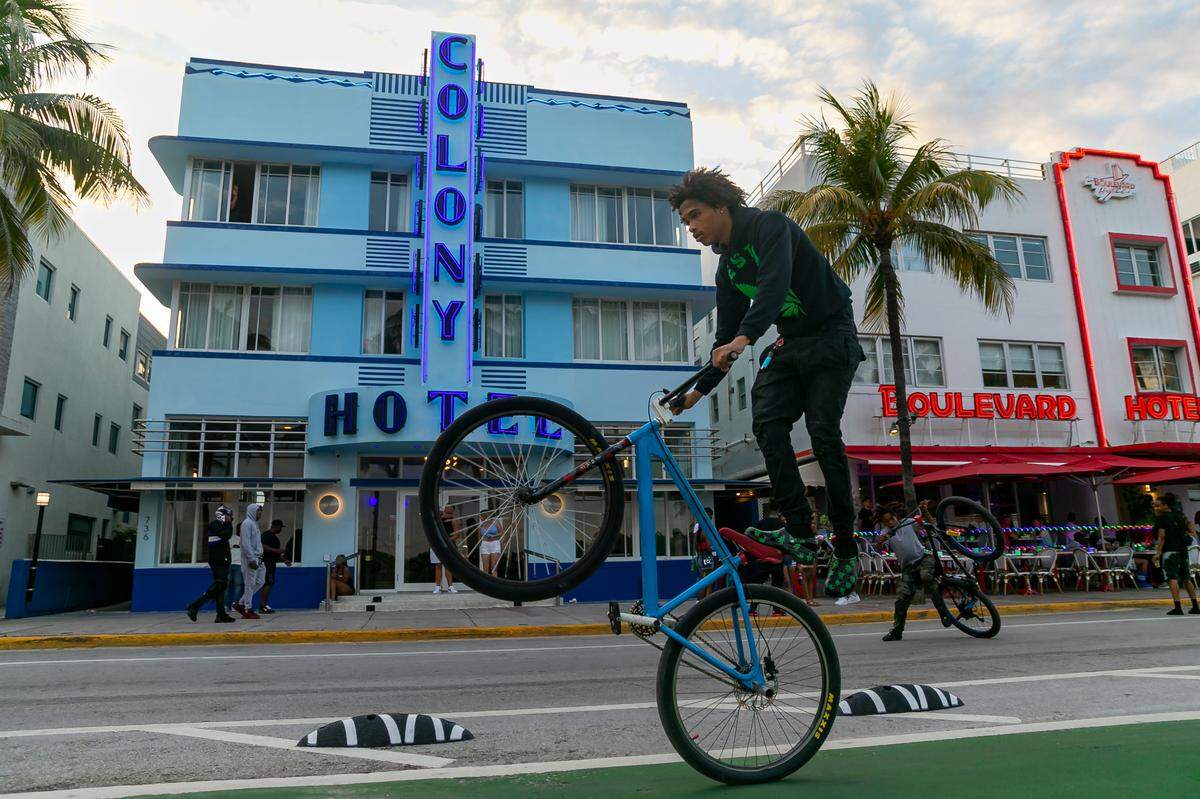 Isaac Martinez performs a wheelie on his bicycle near the Colony Hotel in Miami Beach, Florida on Friday, March 25, 2022. City officials imposed a midnight curfew and forced stores to stop selling alcohol after 6 p.m. The restrictions were set in place after two shootings in Miami Beach the weekend before caused city officials to announce a “state of emergency.”