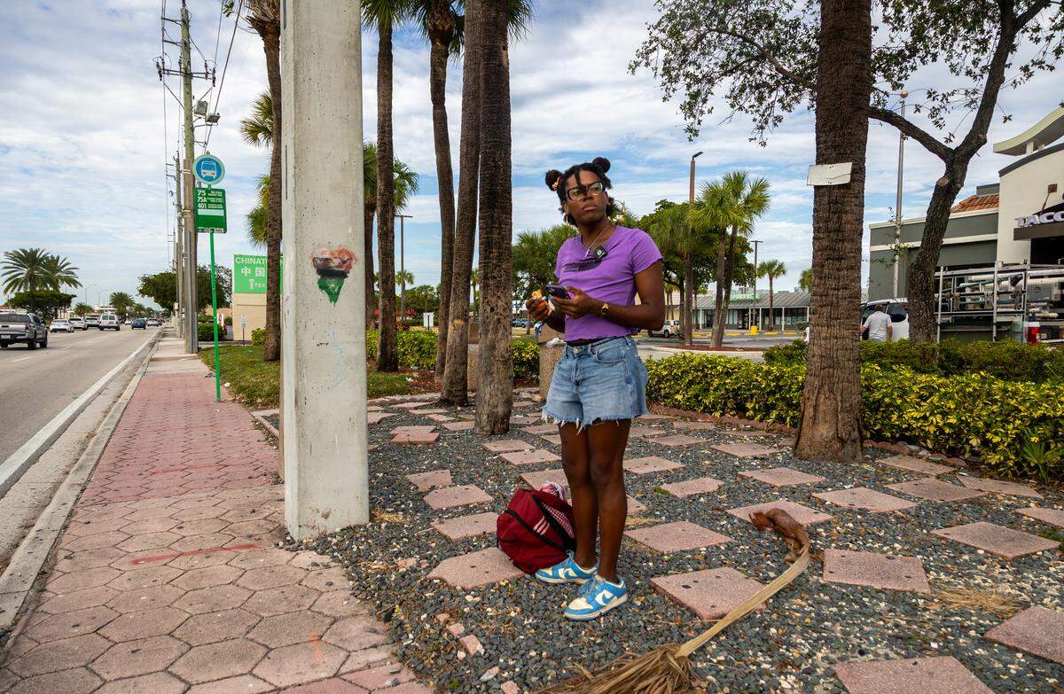 Z Spicer waits at the bus stop, a 15-minute walk from their house in North Miami.