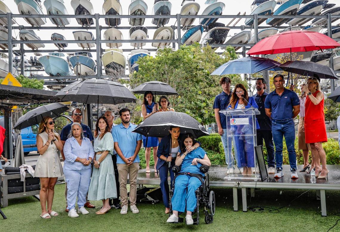 Boating accident survivor Katerina “Katy” Puig, front and center, kisses the hand of her sister, Amanda Puig, as Melissa Fernandez, the mom of Luciana “Lucy” Fernandez, speaks during a press conference commemorating the enactment of Lucy’s Law at Bayshore Club in Miami, Florida, on Wednesday, July 2, 2025. The new state law, which went into effect on Tuesday, toughens penalties for boaters in crashes with serious injuries. It was named after Lucy Fernandez, 17, who died as a result of a boat crash in Biscayne Bay on Sept. 4, 2022.