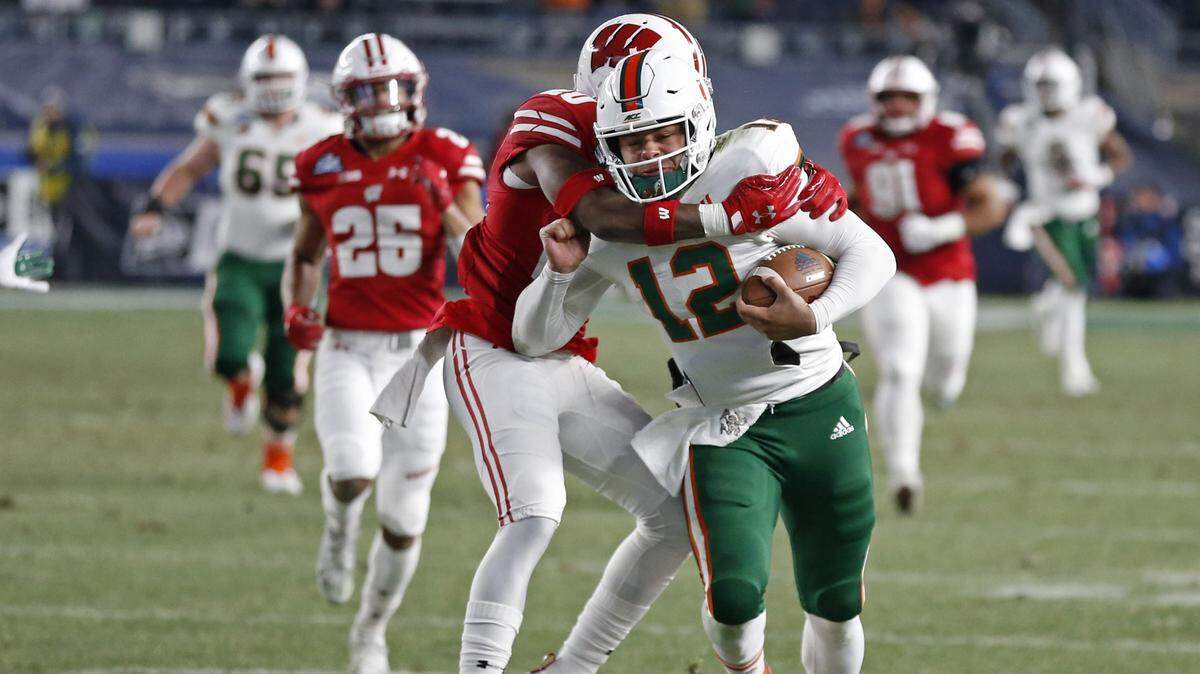 Miami Hurricanes quarterback Malik Rosier (12) runs for a first down as Wisconsin Badgers cornerback Faion Hicks (20) makes the stop in the first quarter as the Miami Hurricanes play against the Wisconsin Badgers in the 2018 New Era Pinstripe Bowl at Yankee Stadium in Bronx, N.Y. on Thursday, December 27, 2018.