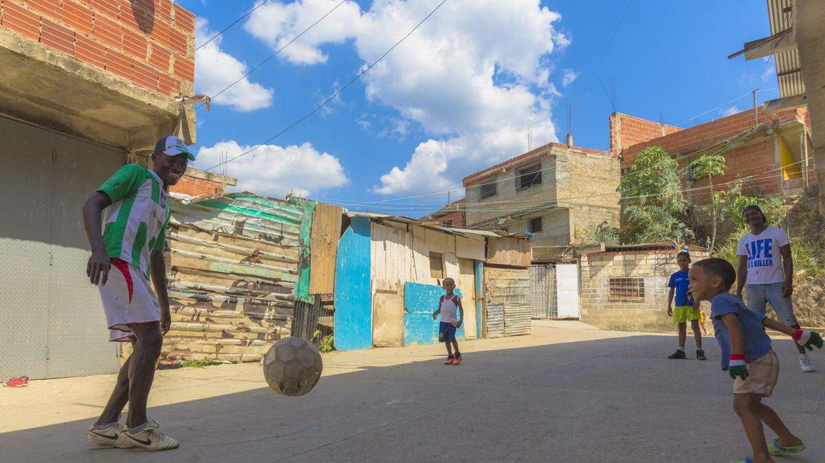 Volunteer soccer trainer Iván Torres plays the game with the children on the street in Petare, a Venezuelan slum near Caracas, before practice begins on the field.  Torres promotes soccer as a tool to prevent delinquency.