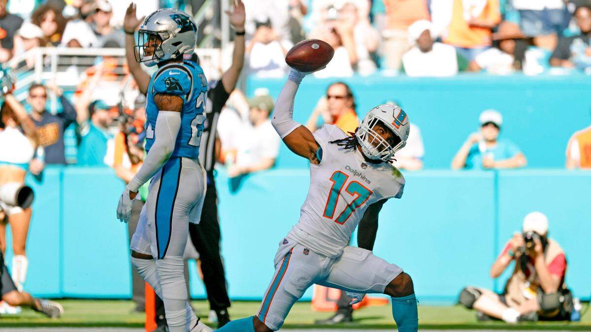 Miami Dolphins wide receiver Jaylen Waddle (17) reacts after scoring a touchdown against Carolina Panthers cornerback Donte Jackson (26) and Panthers middle linebacker Jermaine Carter (4) during the second quarter of an NFL football game at Hard Rock Stadium on Sunday, November 28, 2021 in Miami Gardens, Florida.
