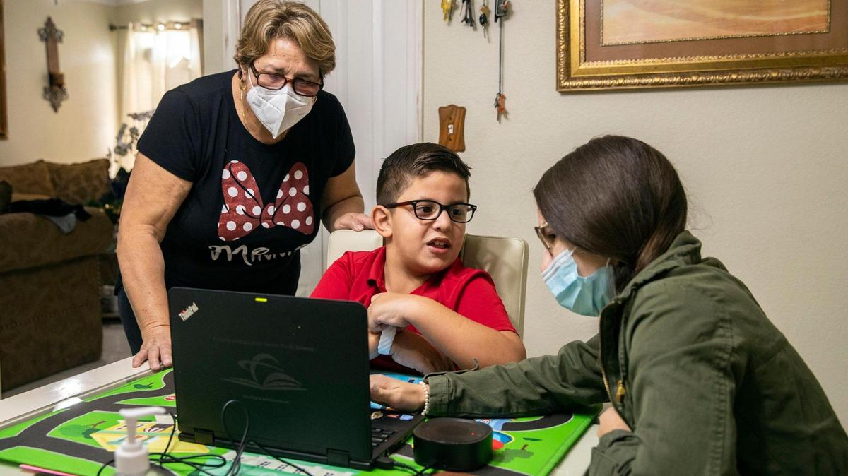 Maria Alfonso, left, joins in to help her grandson David Anaya, 7, as behavioral technician Diana Ramos assists David during a virtual class at home in Miami. Alfonso has been raising David since her daughter died when he was only 3.