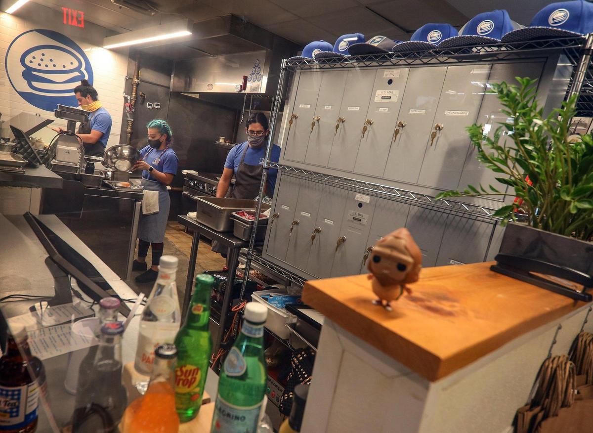Manny Media, left, Keily Vasquez, center, and her husband Mike Mayta, right, prepare lunch inside a tight United States Burger Service kiosk at The Citadel food hall.