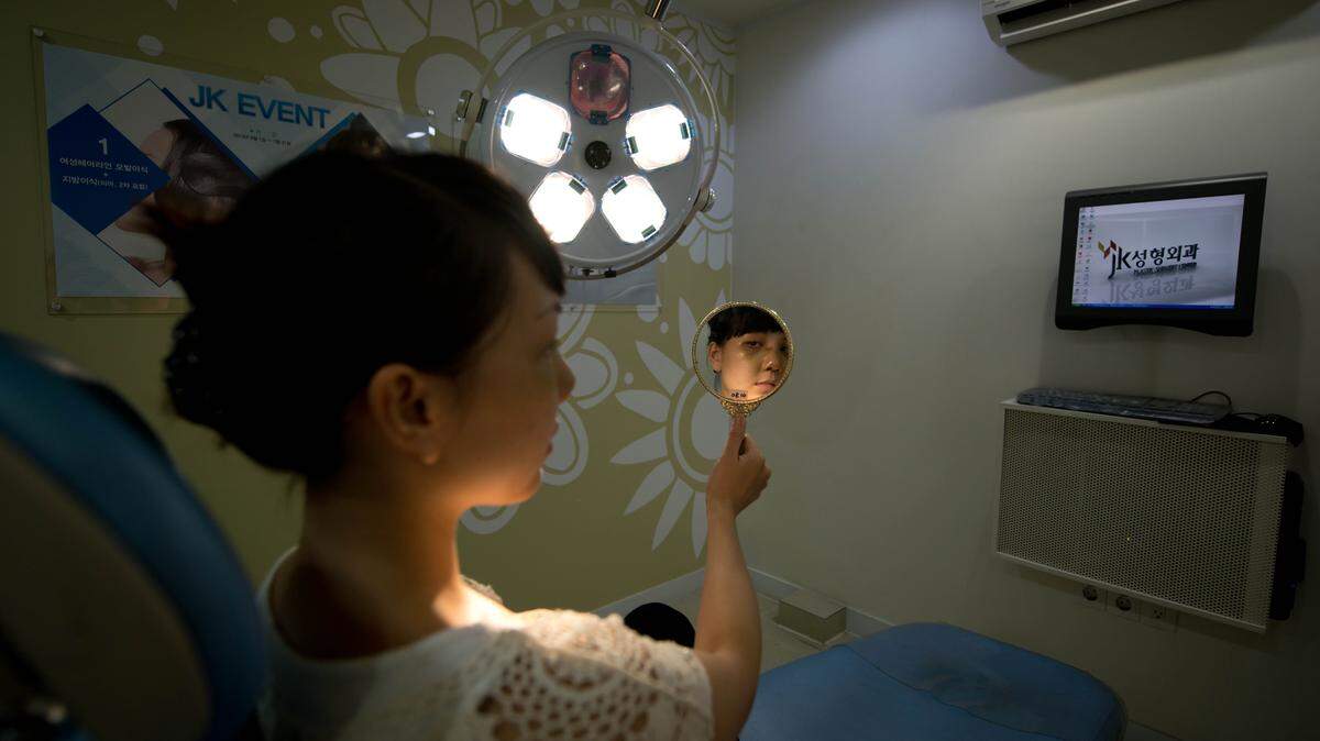 A photo taken on July 15, 2013 shows a Vietnamese-American patient as she checks her appearance four days after undergoing a cosmetic rhinoplasty and eye procedures at the JK Medical Group plastic surgery hospital in Seoul.