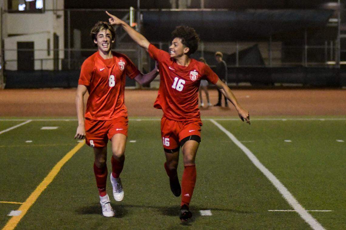 Doral Academy senior Mateo Hincapie (8) and junior Angel Perez (16) celebrate after Perez’s first-half goal in the Firebirds’ regional final win over Dwyer on Wednesday, Feb. 16, 2022, at Doral Academy.