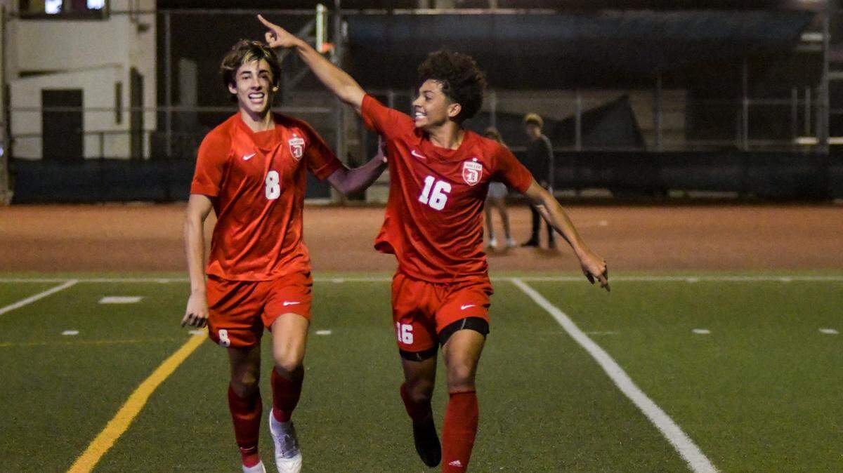 Doral Academy senior Mateo Hincapie (8) and junior Angel Perez (16) celebrate after Perez’s first-half goal in the Firebirds’ regional final win over Dwyer on Wednesday, Feb. 16, 2022, at Doral Academy.