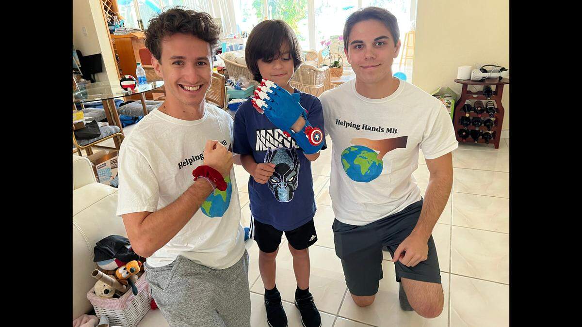 Brothers Jonathan Tamen and David Tamen present Lucca with a 3D printed prosthetic “Captain America” hand that David made for him.