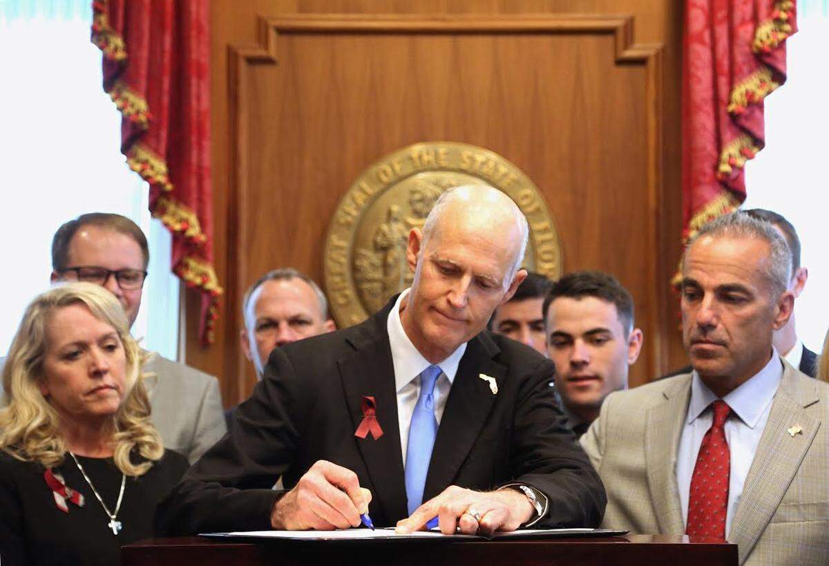 Gov. Rick Scott signs into law gun and school safety legislation on Friday, March 9, 2018 in Tallahassee, Fla. as family members of those who died in the Marjory Stoneman Douglas High School shooting look on. Left is Jennifer Montalto. Right is Andrew Pollack. In back right is Hunter Pollack. (Scott Keeler/Tampa Bay Times/Zuma Press/TNS)