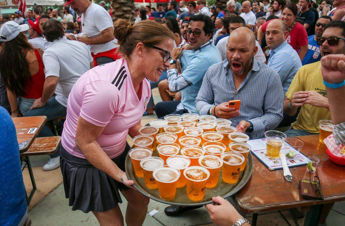 A server brings a tray with cups full of beer to a table as fans watch the game between the United States and Iran during a World Cup watch party at Fritz & Franz Bierhaus in 2022.