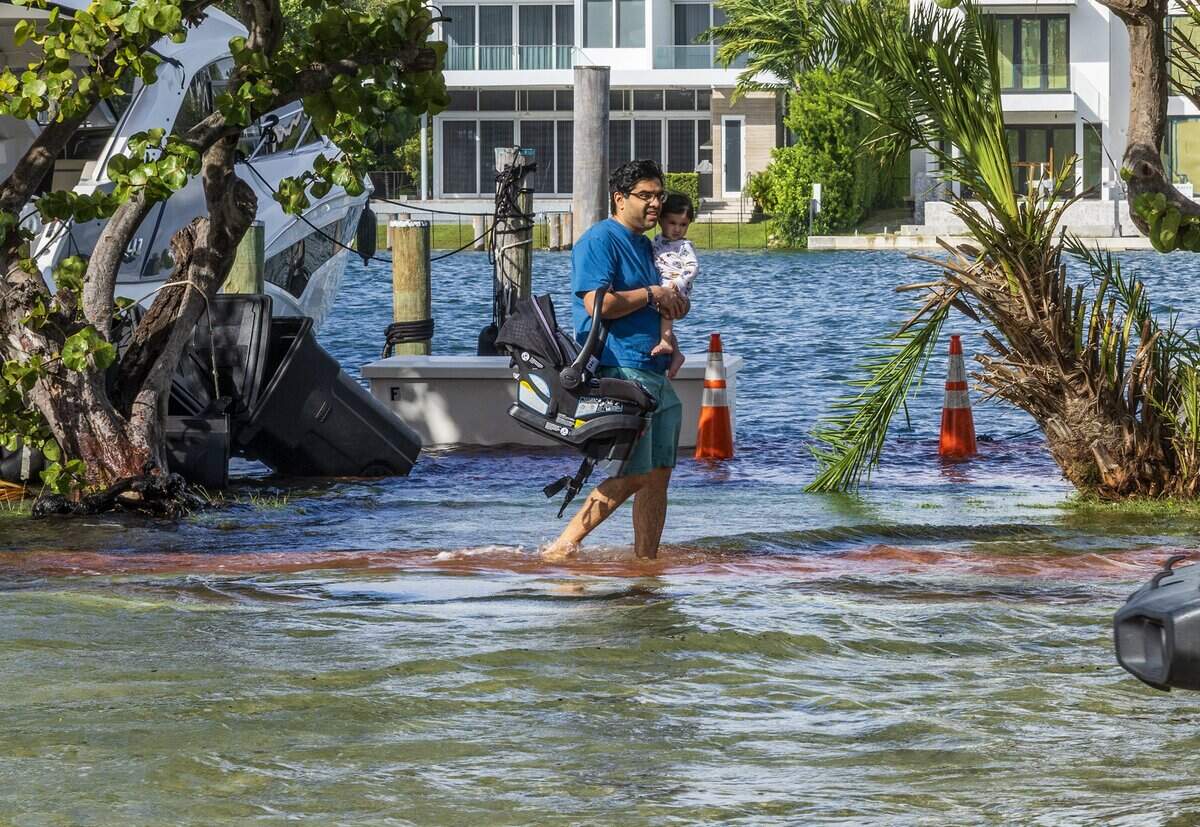 A man holding a child walks barefoot through the flooded streets on Collins Avenue, during king tide in Miami Beach.