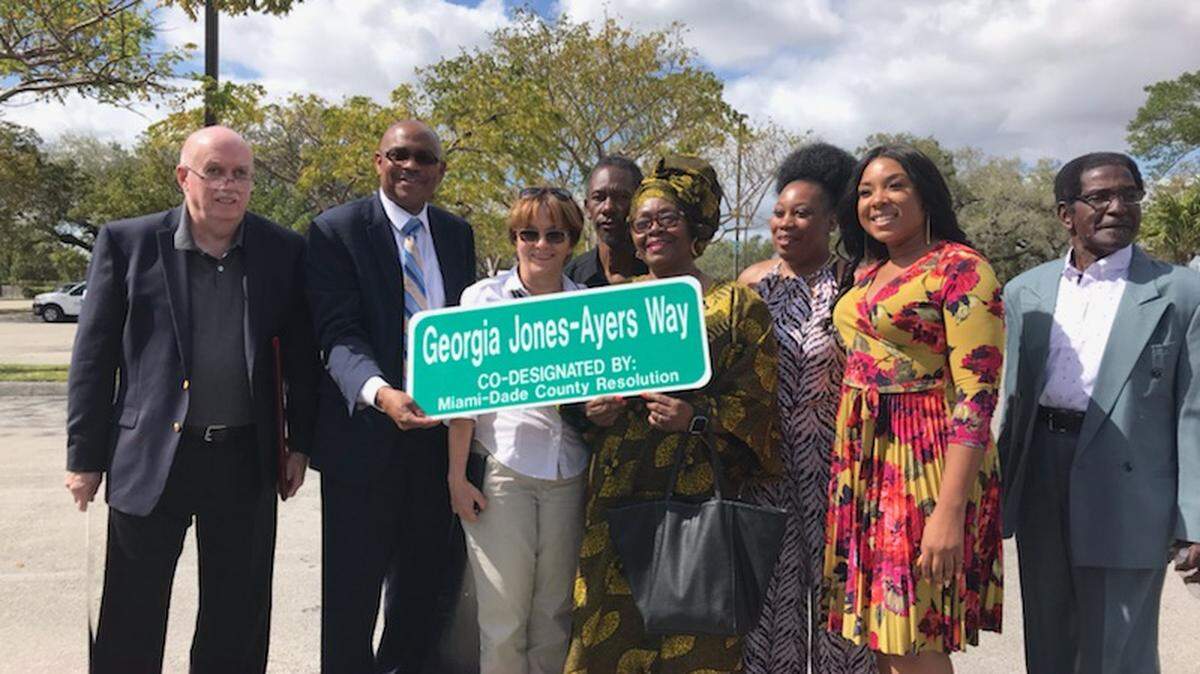 Retired Miami-Dade Circuit Judge Thomas K. Petersen, co-founder of The Alternative Programs; program Executive Director Kenneth M. Kilpatrick; program employees Margarita Prawl, Jean Francois, Cynthia Rolle, Reashawnda Jenkins, Faith Elibert (Georgia Jones-Ayers’ granddaughter); and Earl Bethel with the newly unveiled Georgia Jones-Ayers Way street sign.