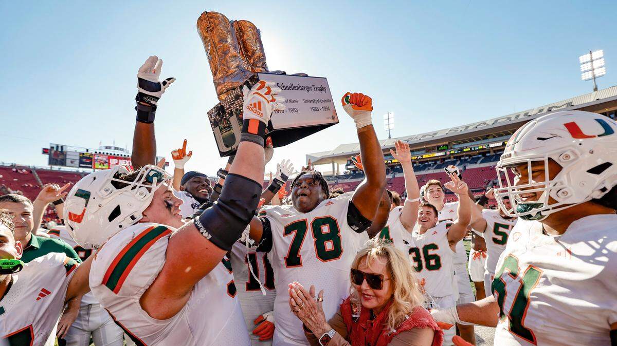 Miami Hurricanes left guard Matt McCoy (78) and teammates celebrate as Carpenter holds up the Howard Schnellenberger trophy as the winner against rival Louisville Cardinals in an NCAA football game at L&N Federal Credit Union Stadium in Louisville, Kentucky on Saturday, October 19, 2024. Schnellenberger’s widow, Beverlee, is in front joining celebration.