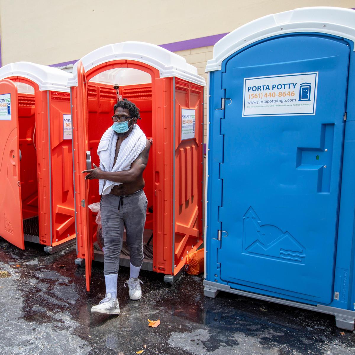 Malachi Woumans, 42, walks out of the porta potty shower unit after finishing a shower during an extended services event for the unhoused, hosted by Dr. Armen Henderson, Dream Defenders and a coalition of community organizations and medical providers at St. John Institutional Missionary Baptist Church in Overtown, Florida on Friday, April 24, 2020.