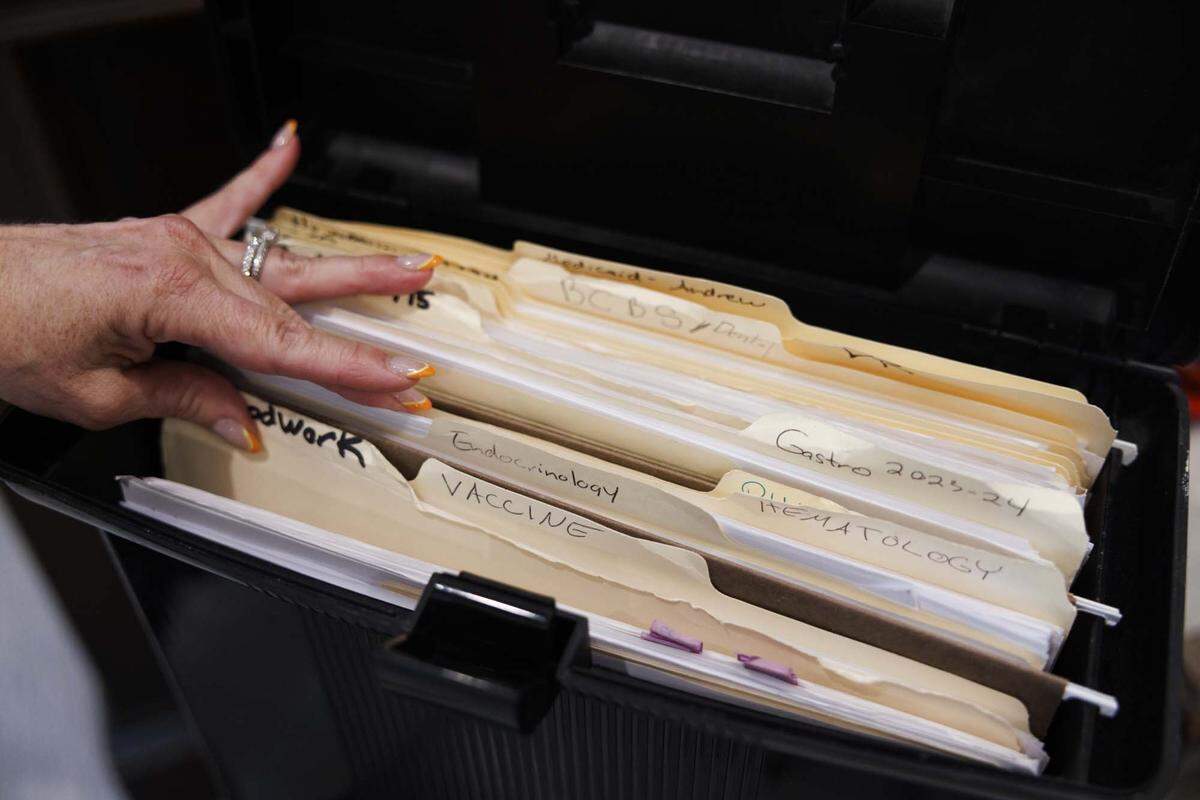 Anne Davies-Vicino flips through the box of files she takes with her to doctors appointments with her son, Andrew Vicino, in her home on Thursday, May 21, 2026, in Boca Raton, Fla. She now has to take her son to different hospitals across South Florida to care for his rare genetic condition because Joe DiMaggio Children's Hospital, which had all of his doctors in one place, is no longer in-network with Florida Blue due to ongoing contract disputes.