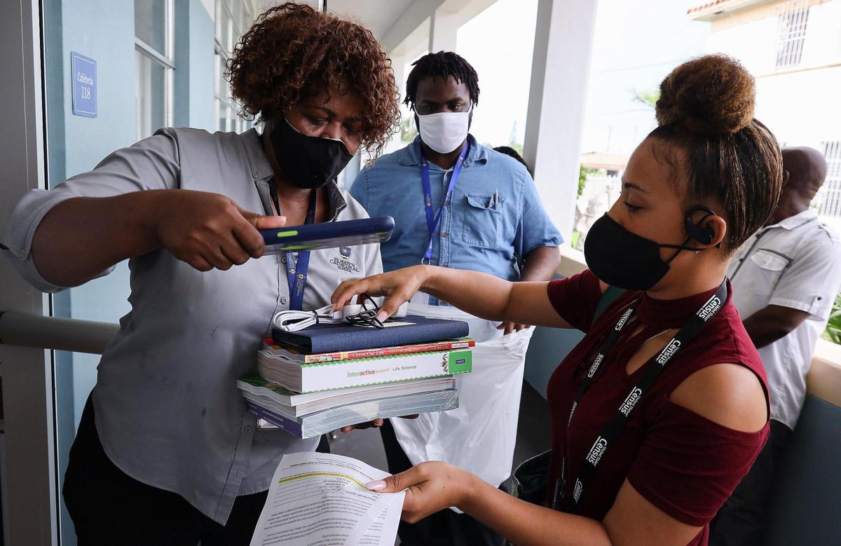 Teacher Michaelle Joseph, left, gives books and iPads to Louna Dorcelien, right, at St. Mary’s Cathedral School on Wednesday, Aug. 19, 2020, in Miami’s Little Haiti neighborhood. Teacher Jeffrey Phillipe, center, waits to place the items in a bag. The supply distribution event was to help prepare students for the first day of online learning.