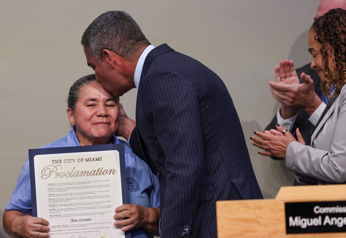 At the last Miami City Commission meeting, Mayor Francis X. Suarez, center, kiss the head of Alba Cordovi, left, a beloved city employee, after being presented a city proclamation for strong work ethic and kindness on Thursday, December 11, 2025, at City Hall in Miami, Florida.