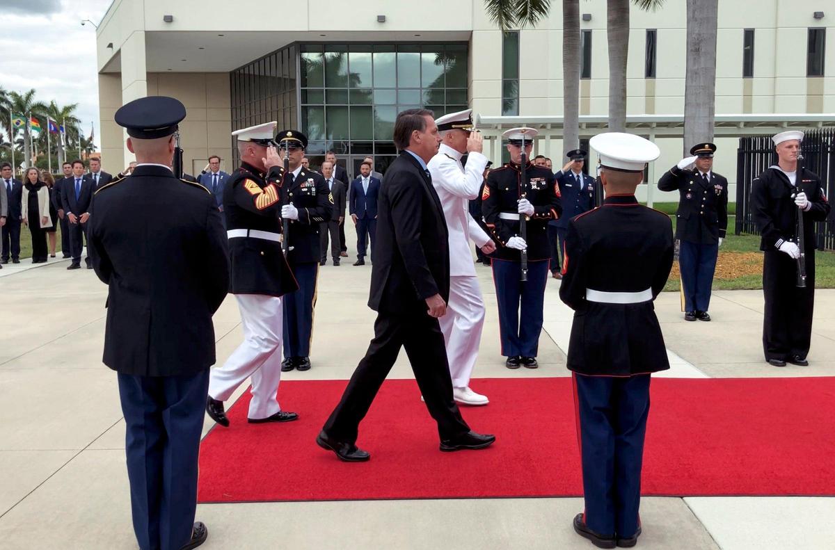 Brazilian President Jair Bolsonaro, center, walks along side of U.S. Navy Adm. Craig Faller, commander of U.S. Southern Command, on the ceremonial red carpet during the historic first visit to the U.S. Southern Command to be present for the signing of a bilateral Agreement on Research Development, Test, and Evaluation Projects on Sunday, March 8, 2020 in Doral, Florida.