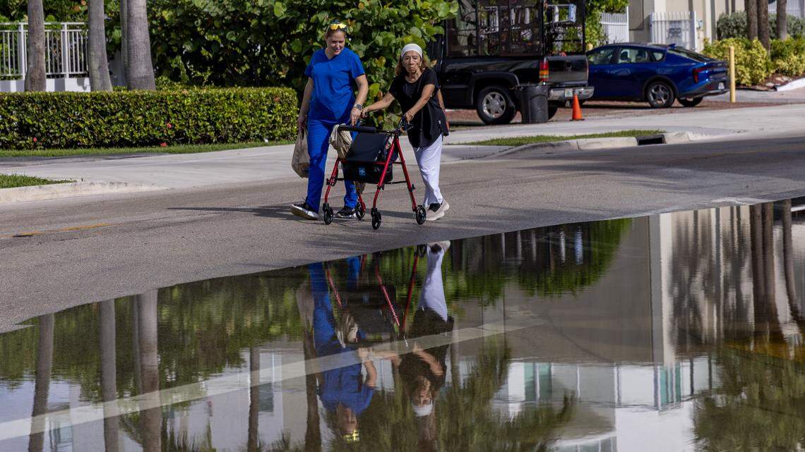 Floodwaters from high tide cover part of the intersection of North Bay Road and 180th Drive as two people walk in the middle of the road to avoid the sidewalk in Sunny Isles Beach, Fla., on Monday, Oct. 6, 2025.