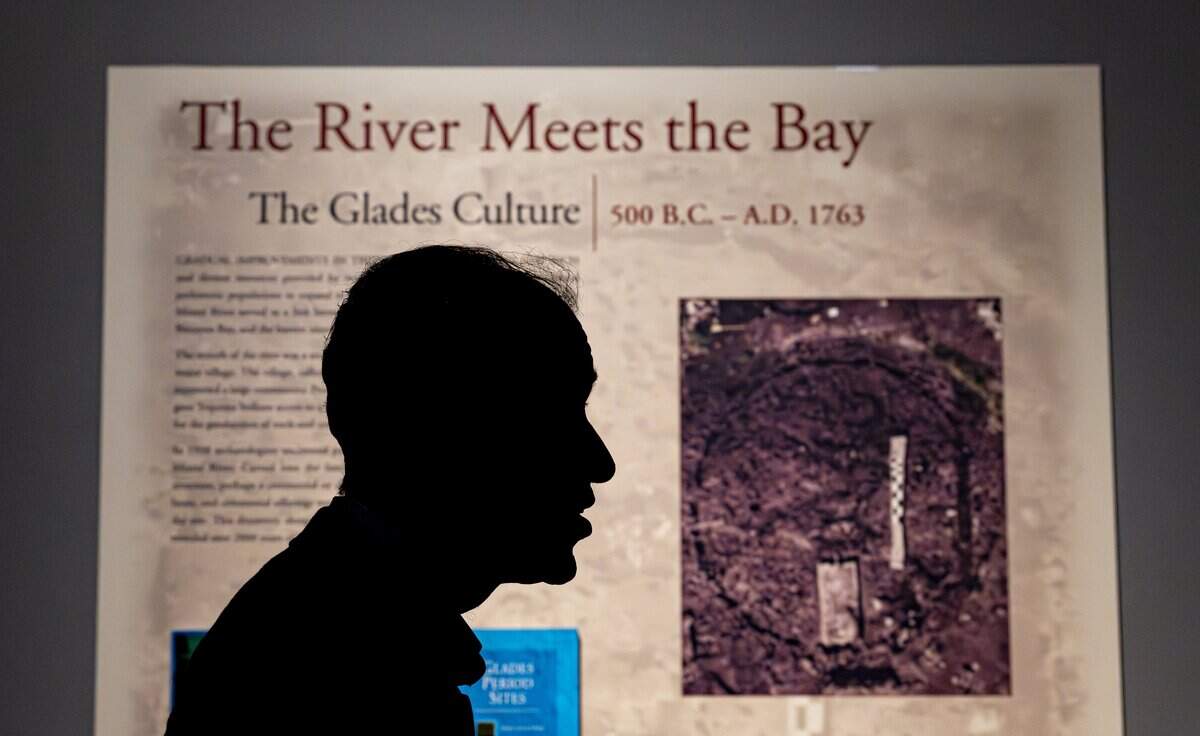 Paul George, resident historian at the Museum of Miami, is silhouetted against an exhibition panel on South Florida’s prehistoric indigenous people illustrated with an overhead photo of the 2,000-year-old Miami Circle, taken just after its 1998 discovery at the mouth of the Miami River.