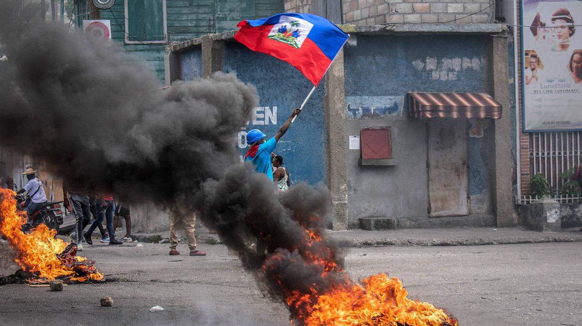 A man waves the Haitian flag, as street fires burn, to ask for peace. The residents of Carrefour-Feuilles took to the streets to denounce gang violence and ask the government curb their abuses. The police dispersed them with tear gas.