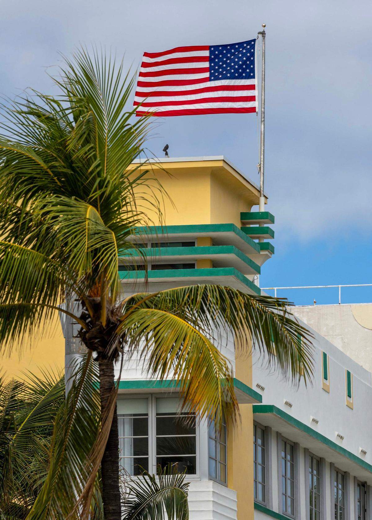 An American flag waves high above the palms and Art Deco buildings during the 16th Annual Veterans Day Parade off Ocean Drive on Monday, Nov. 11, 2024, in Miami Beach, Fla.