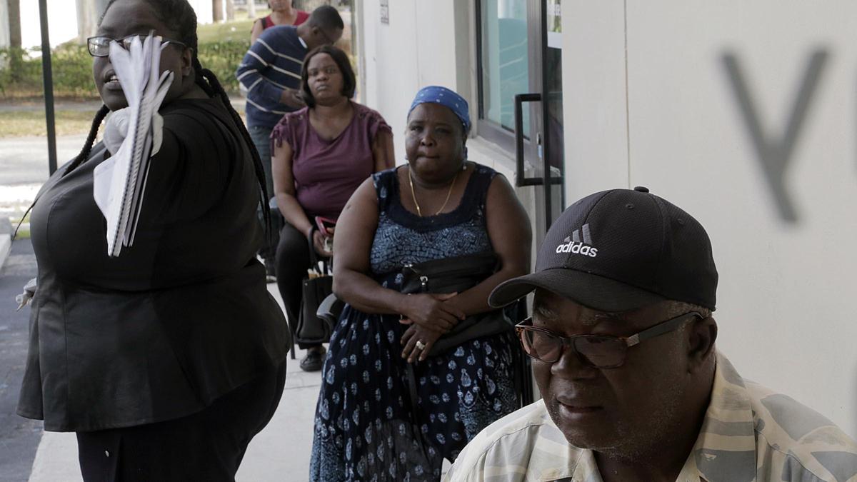 Rose Mainville, Youth and Family Advocacy Coordinator for Sant La Haitian Neighborhood Center (left) directs people to the door as others wait in line to come into the center on March 24.. Sant La is helping laid off workers file for unemployment.
