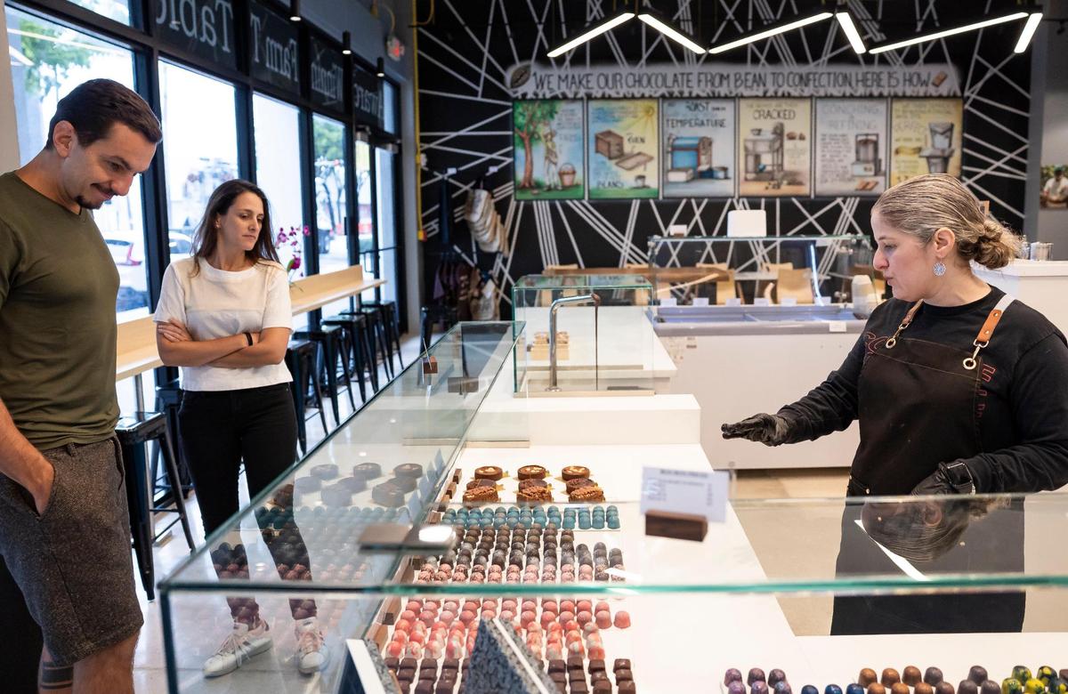 Carolina Quijano, right, founder of Exquisito Chocolates, talks with customers Gabriel Gasparini and Laylla Florez as they decide what to order at the new Calle Ocho factory.