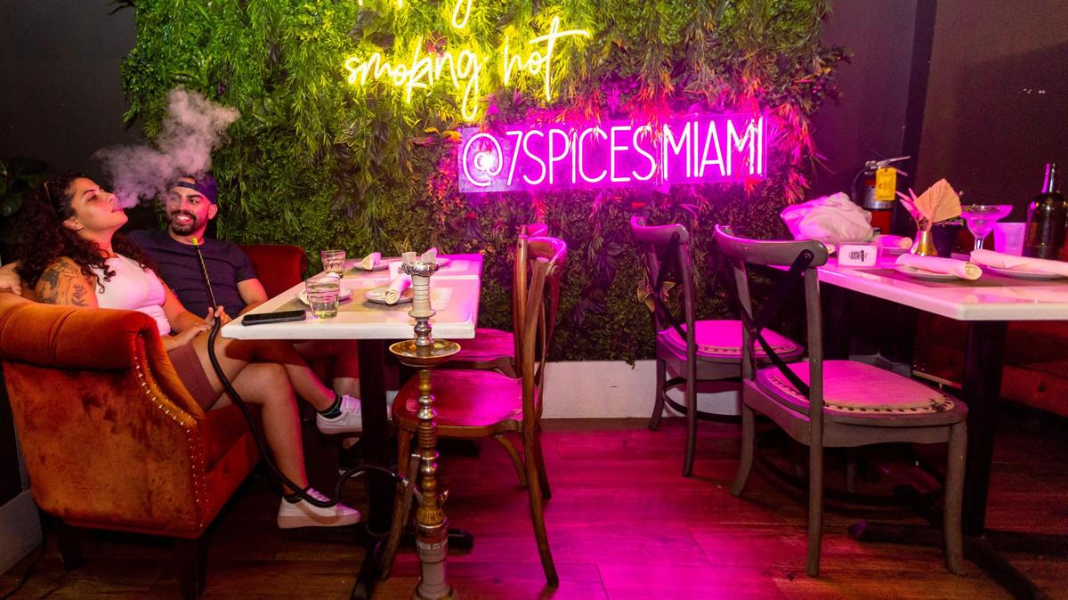 West Palm Beach resident Germena Hemai, 21, left, smokes hookah with her boyfriend Josue Capellan, 29, at 7 Spices on Lincoln Road in Miami Beach, Florida, on Thursday, Dec. 1, 2022. In October, Miami Beach implemented a new system to regulate sidewalk cafes that bans hookah on public property, meaning shops like 7 Spices can no longer serve it outdoors.