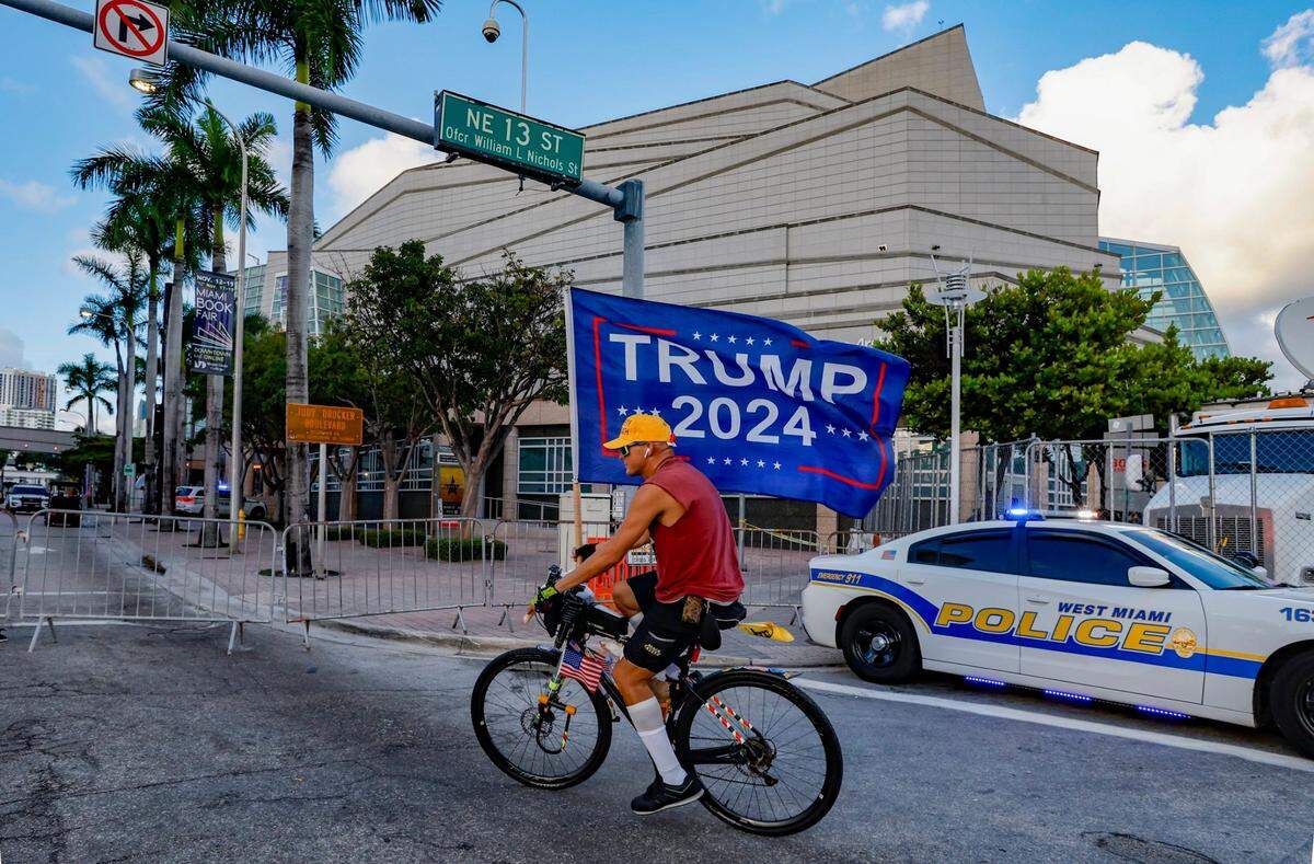 Former President Donald Trump supporter, Chaunce O’Connor, 41 of Miami, carries a flag as he rides past the Adrienne Arsht Center for the Performing Arts of Miami-Dade County just hours before the start of the third Republican presidential primary debate on Wednesday, November 8, 2023, in downtown Miami, Fla.