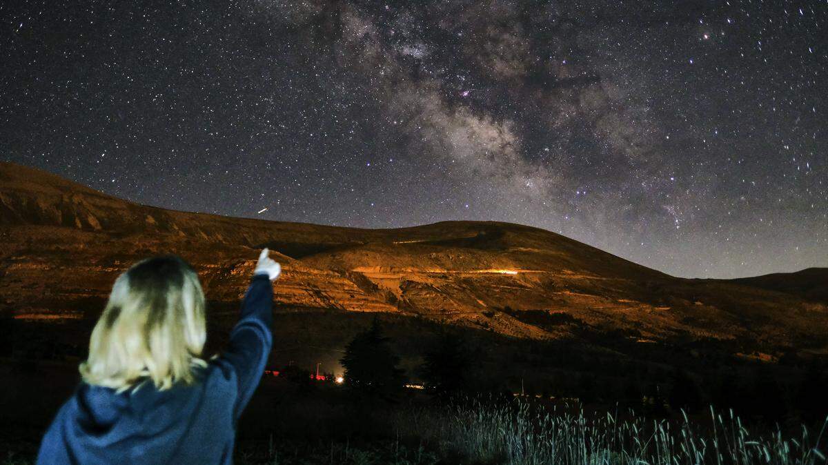 This long-exposure picture taken early on July 21, 2022, shows a girl pointing towards the Milky Way galaxy in the sky above the cedar forest reserve, also known as the Cedars of God, near the town of Bcharre in mount Lebanon, north of the capital Beirut.