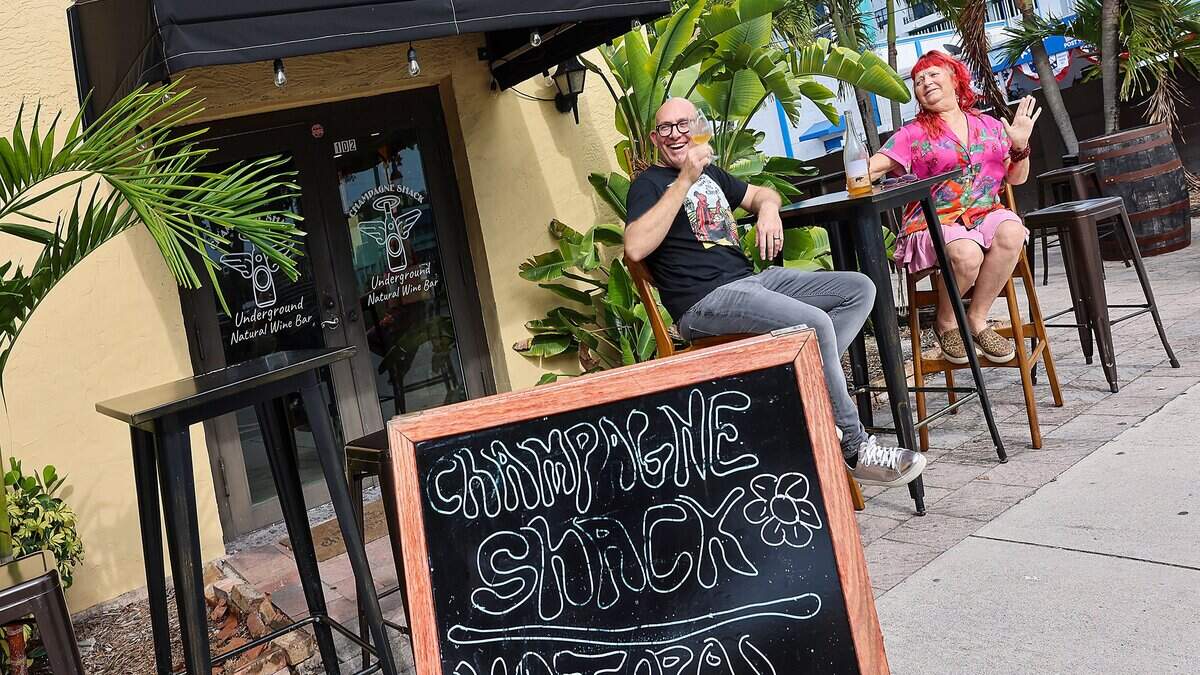 Stephen Eisel, left, and Ysee Gaudel-Eisel, right, enjoy a glass of wine while greeting locals outside their wine bar, Champagne Shack, in Hollywood, Florida, Wednesday, June 10, 2026. Champagne Shack is a small, independently owned wine bar that draws local residents with its casual atmosphere. The bar regularly features food vendors on weekends, pop-up events with area restaurants, yoga sessions, a wine club, and live music or DJ performances in its courtyard on Fridays and Saturdays.