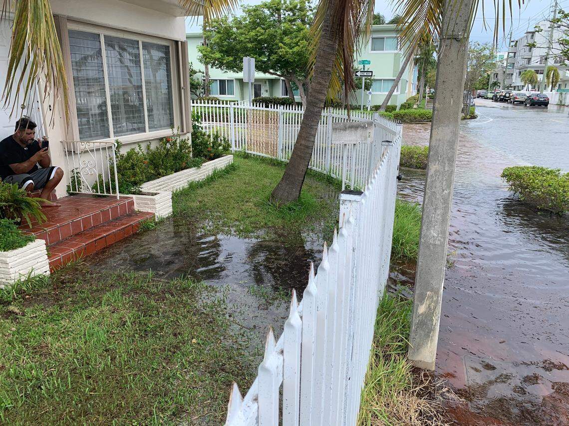 A man smokes a cigarette and video chats with a friend on his porch, the only dry spot on his street after a King Tide-related flood. The corner of 82nd Street and Crespi Boulevard in Miami Beach flooded completely on Oct. 19, 2020, during a high tide.