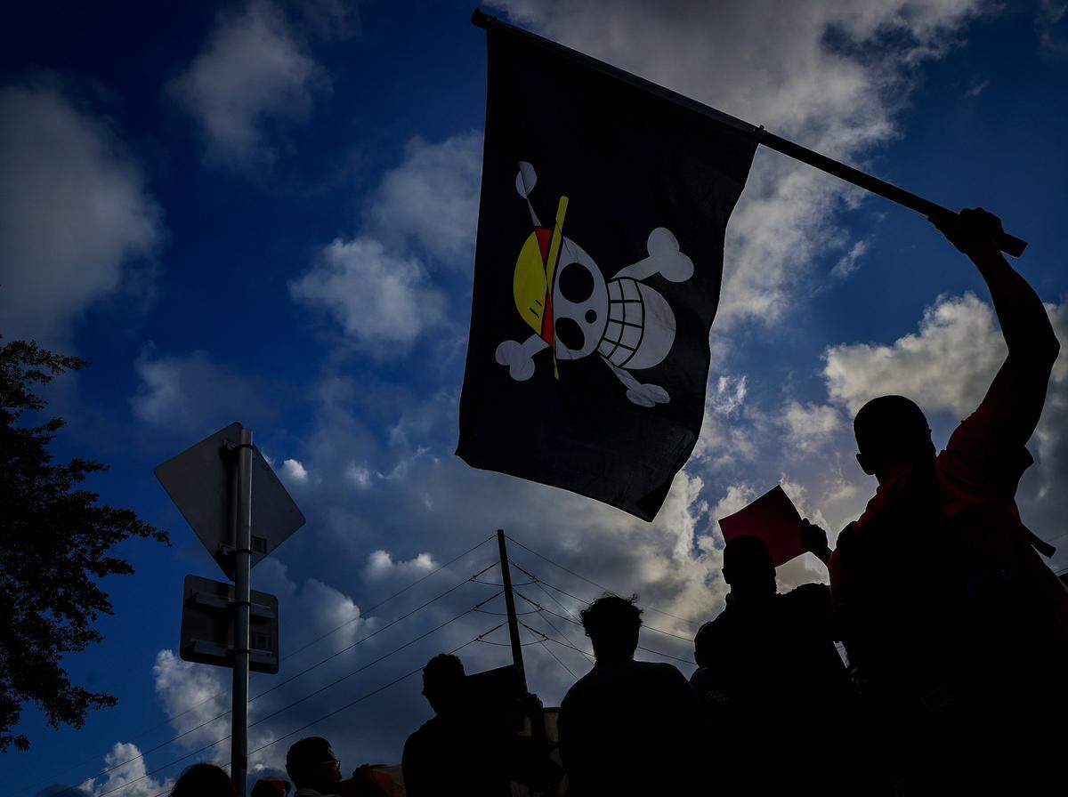 Protestor who goes by the name “Goose,” right, waves the “One Piece” pirate flag as a small group gathered around the mall entrance, wielding bright signs that conveyed messages calling for increased accountability and transparency from the tech giant on Tuesday, March 3, 2026 at the entrance of Aventura Mall in Aventura, Florida.