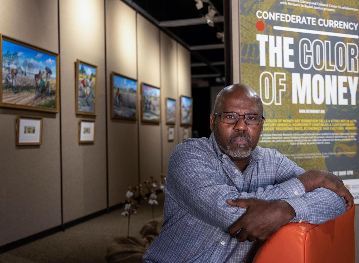 Dwayne Rayner, executive director of Partners in Racial Justice, is photographed alongside artist John Jones’ exhibition “The Color of Money.” The new exhibition at the African-American Research Library and Cultural Center explores the connection between America’s economy and slavery.
