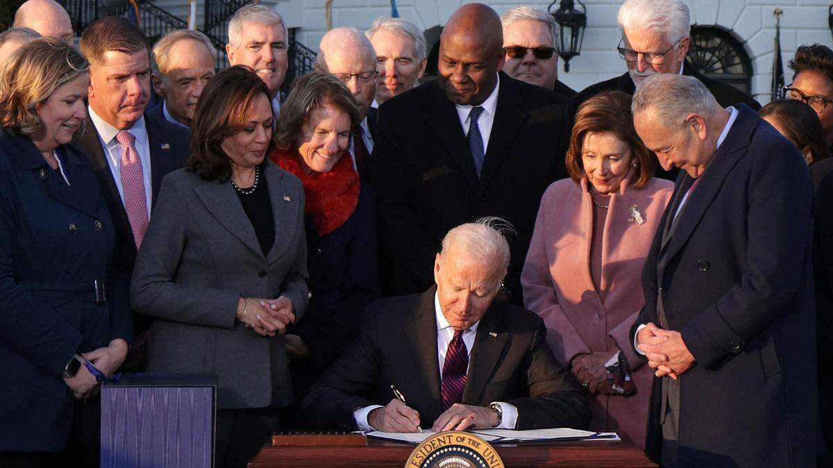President Biden signs the Infrastructure Investment and Jobs Act, as lawmakers and Cabinet members watch.