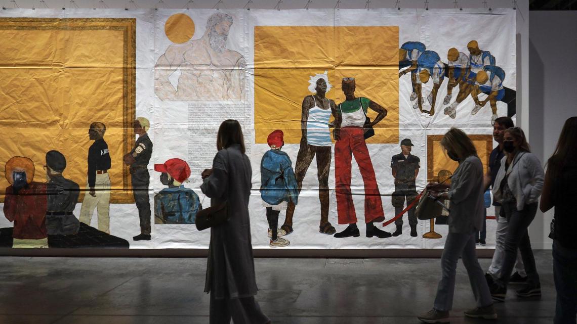 An Art Basel VIP walks and keeps her eyes on Maxwell Alexandre’s sweeping “Untitled (New Power Series)” during a preview at the fair’s Meridians sector, which focuses on large-scale work. The 2021 piece is made of latex, shoe polish, bitumen, henna, dye, charcoal, graphite, acrylic and Xerox transfers onto brown paper.