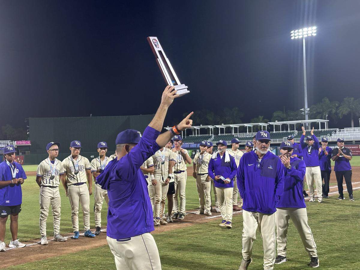 True North baseball coach Adrian Nieto holds up the Class 2A state runner-up trophy and acknowledges their fans after Tuesday’s state championship game at Hammond Stadium in Fort Myers, Fla.