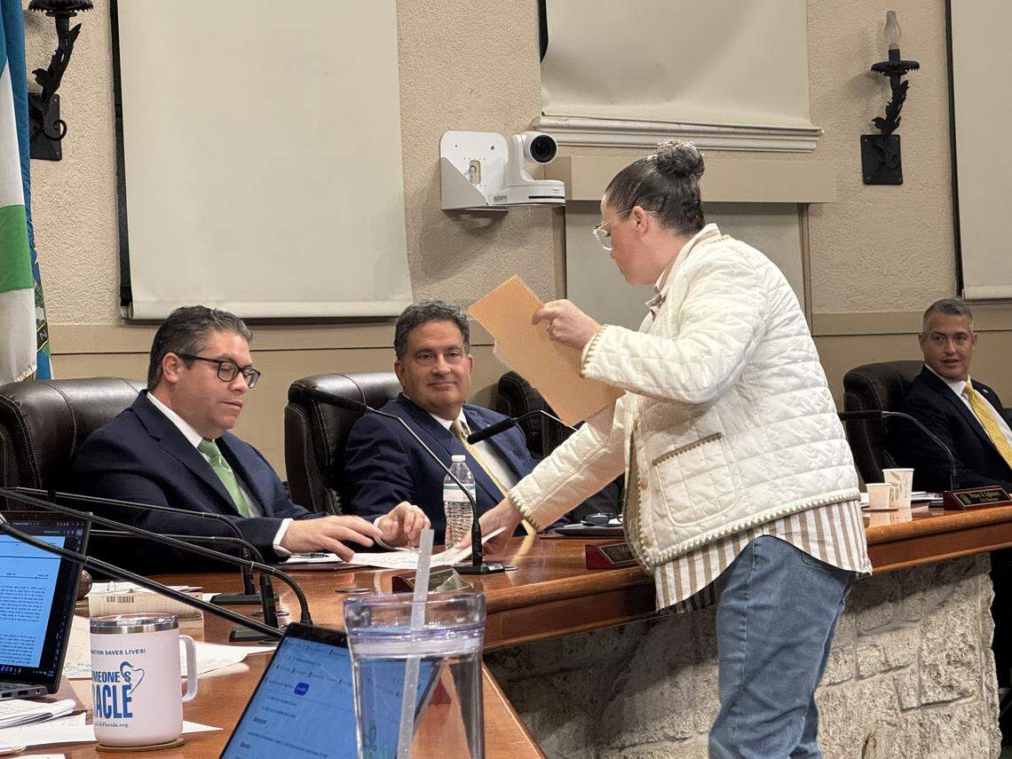 Coral Gables resident Mary Powell gives Commissioner Ariel Fernandez and other members of the commission a copy of a map showing the locations of people who signed a petition supporting an off-leash dog park at a city-owned grassy area at the corner of Segovia Street and University Drive during a City Commission meeting on Tuesday, Jan. 13, 2026.