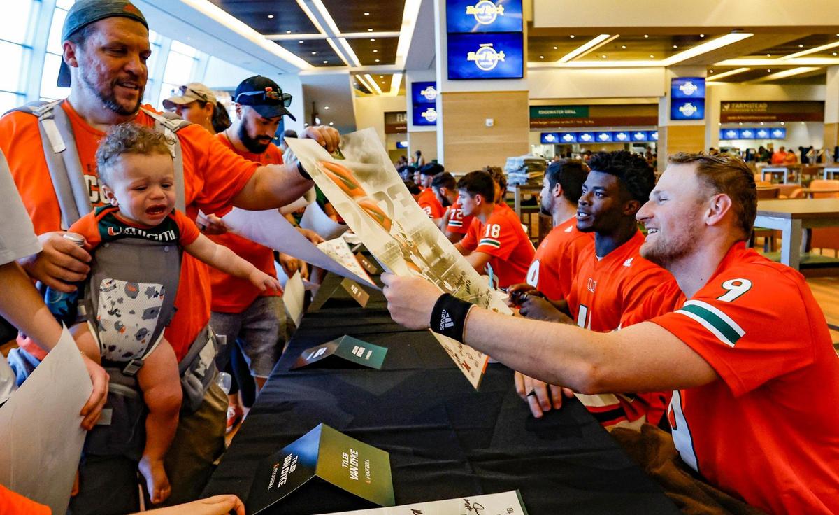 Hurricanes quarterback Tyler Van Dyke reaches for a poster from Brett Conger for signing during the University of Miami’s annual CanesFest at Hard Rock Stadium.