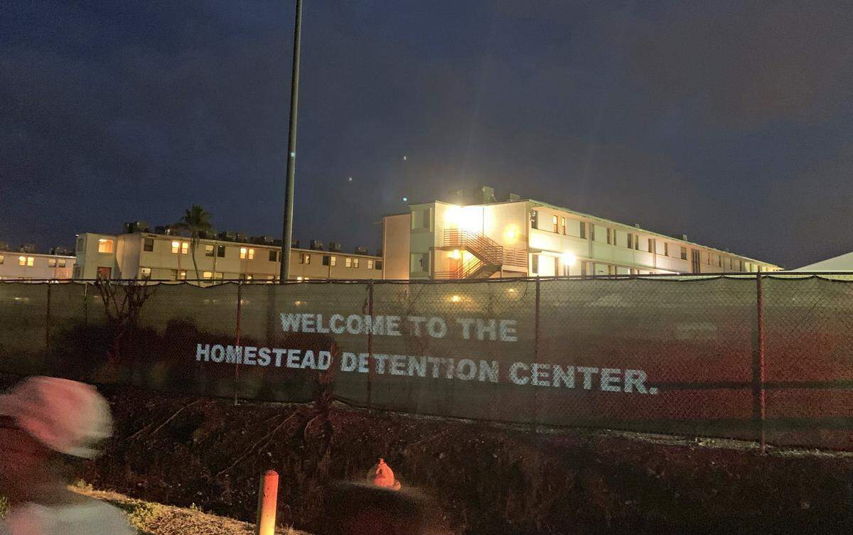 An artist projects messages on the fencing outside the Homestead child detention center on Friday during a protest at the shelter. The messages included excerpts of a legal filing describing conditions inside the center, which currently houses 1,750 minors.
