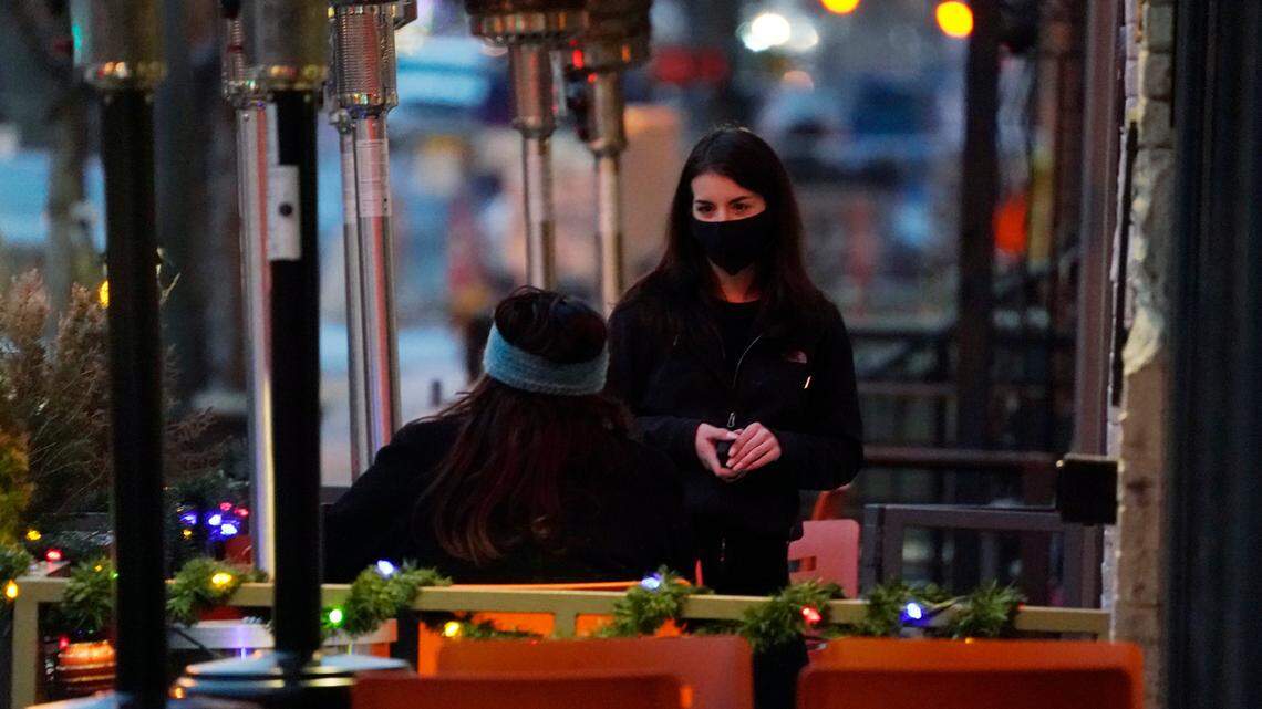 A server wears a face mask while tending to a patron sitting in the outdoor patio of a sushi restaurant in Denver on Dec. 28.