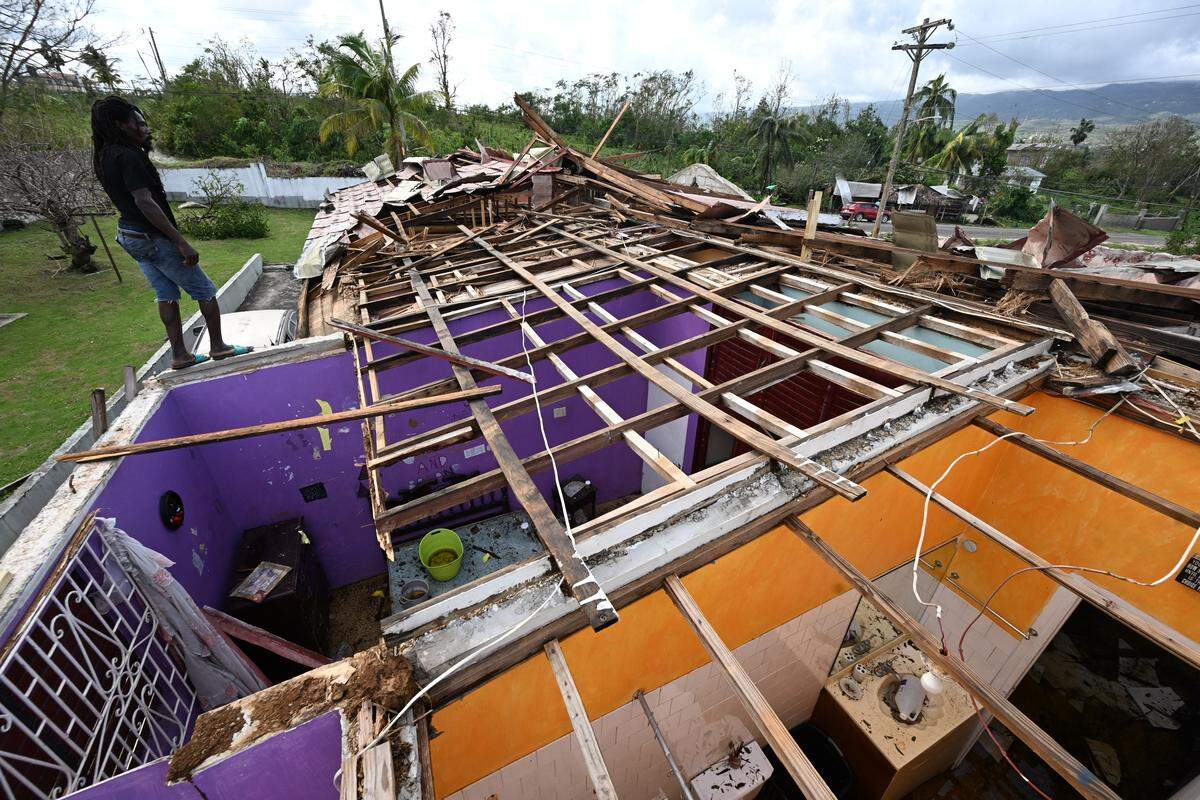 A man stands on what is left of the roof of his neighbor following the passage of Hurricane Melissa, in longwood, St Elizabeth, Jamaica on October 29, 2025. Hurricane Melissa ripped up trees and knocked out power after making landfall in Jamaica on October 28, 2025 as one of the most powerful hurricanes on record, inundating the island nation with rains that threaten flash floods and landslides. 