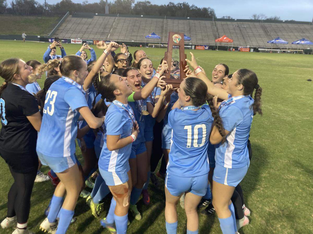 Lourdes’ soccer players celebrate with the trophy after winning the Class 6A girls’ soccer state championship Saturday at Spec Martin Stadium in DeLand, Fla.